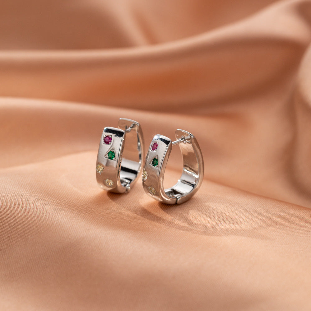 Silver tone huggie hoop earrings with colored stones on peach fabric