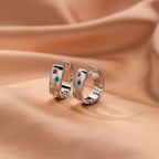 Silver tone huggie hoop earrings with colored stones on peach fabric