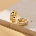 Gold tone huggie hoops with colored stones on a stone block
