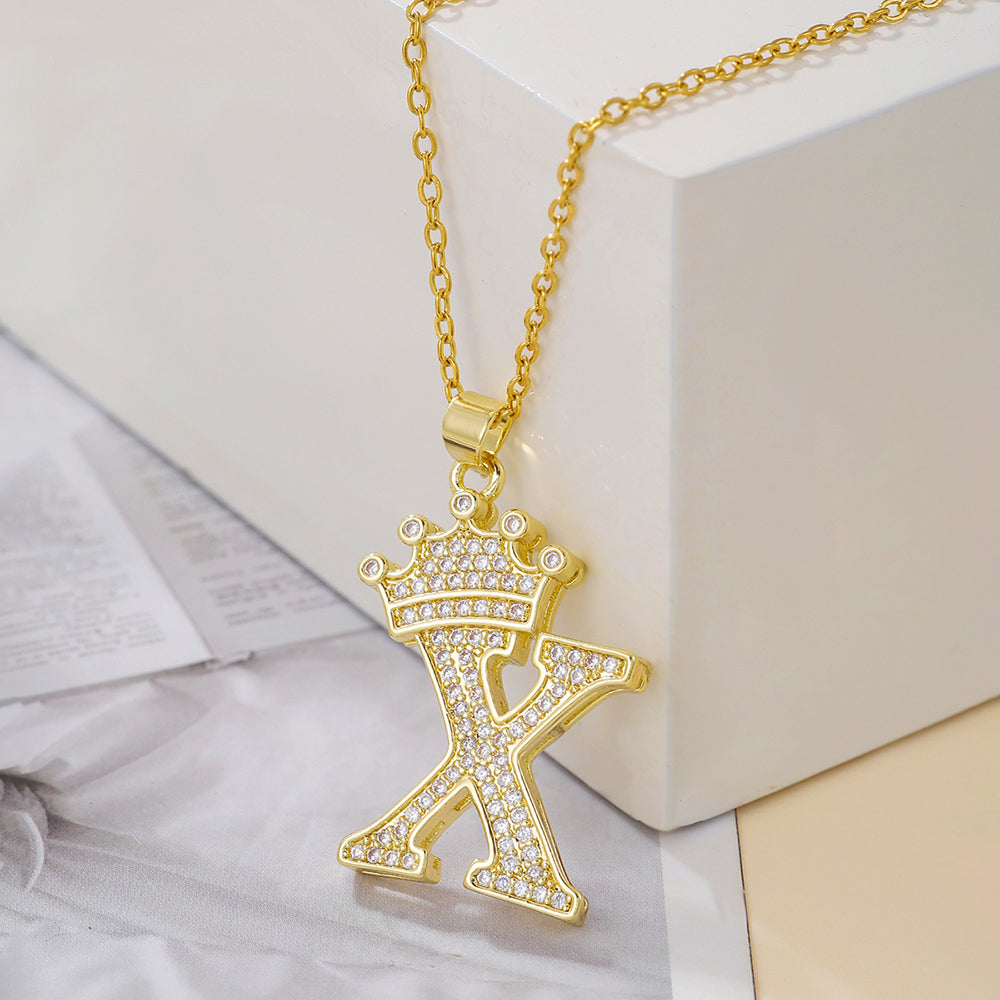 Gold tone crown letter X pendant necklace on a white block