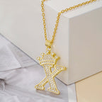 Gold tone crown letter X pendant necklace on a white block