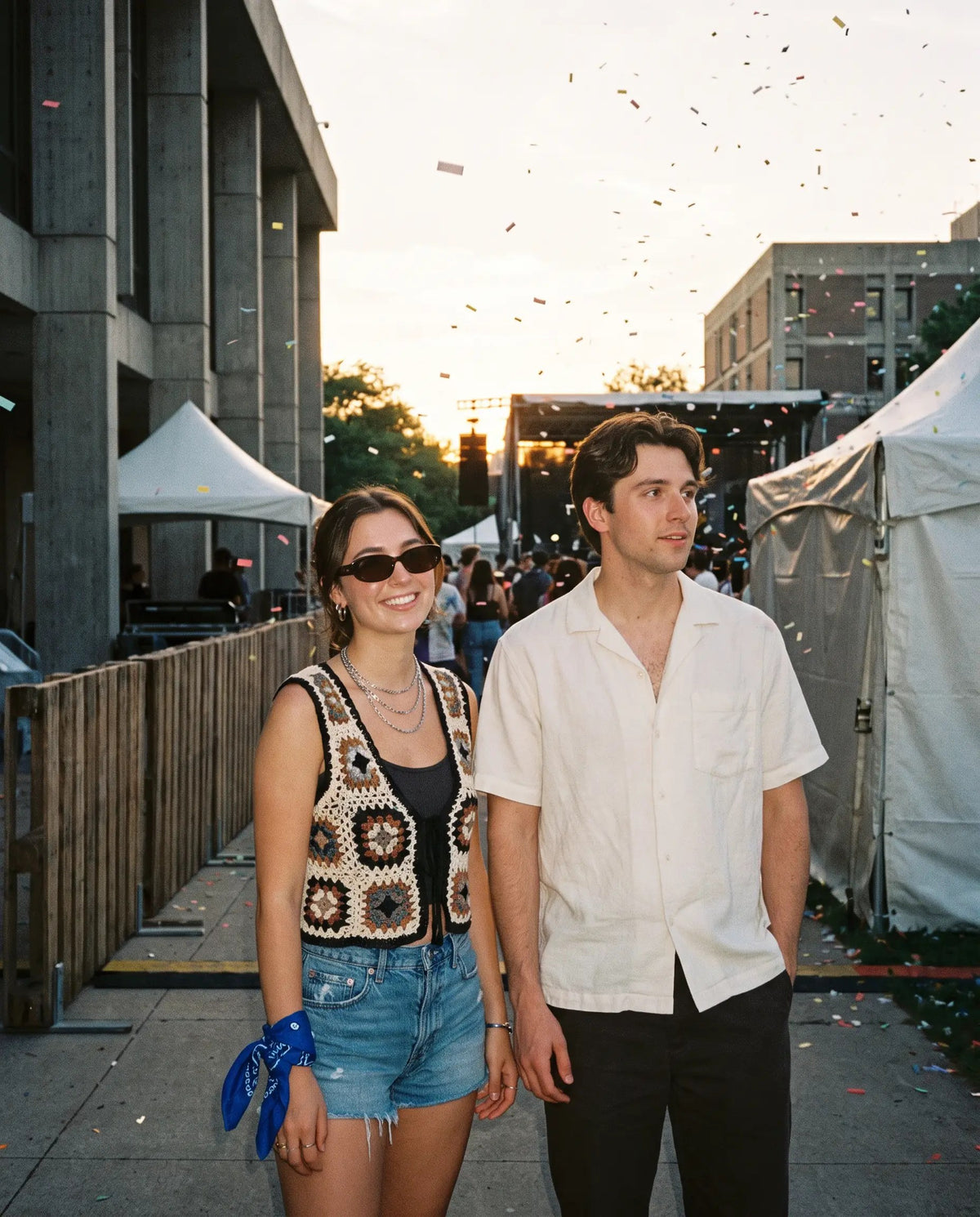 Two friends at an outdoor campus festival: crochet vest, denim shorts and bandana; white camp-collar shirt and black trousers